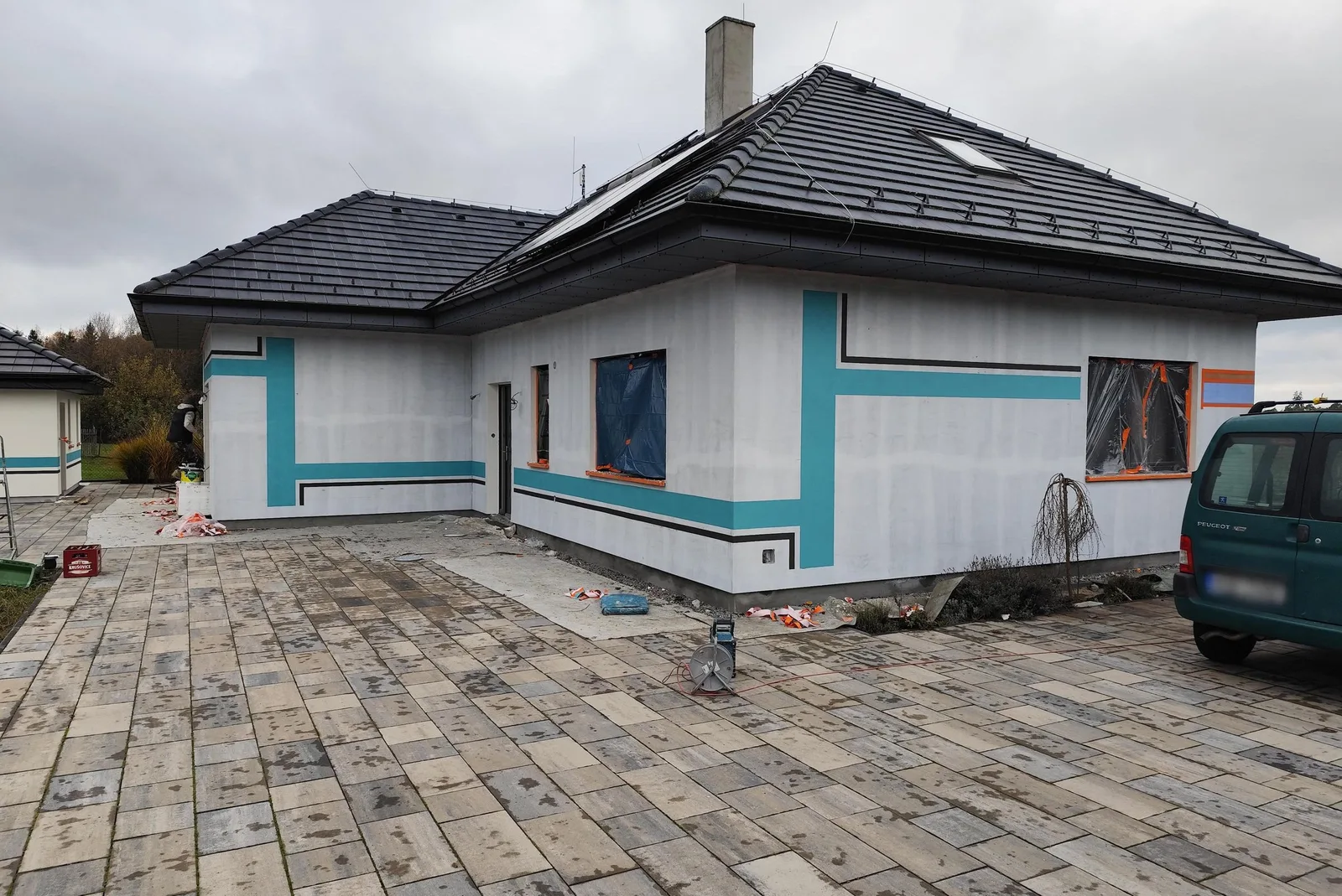 Přízemní dům během zateplování: bílá stěrka na izolantu, okna zakrytá fólií a&nbsp;nová zámková dlažba před domem