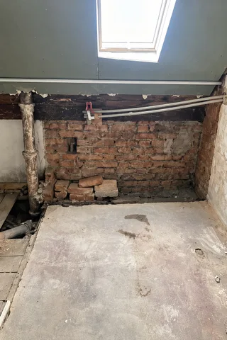 Cihlová zeď pod střešním oknem, kolem ní nové šedé chráničky pro rozvody